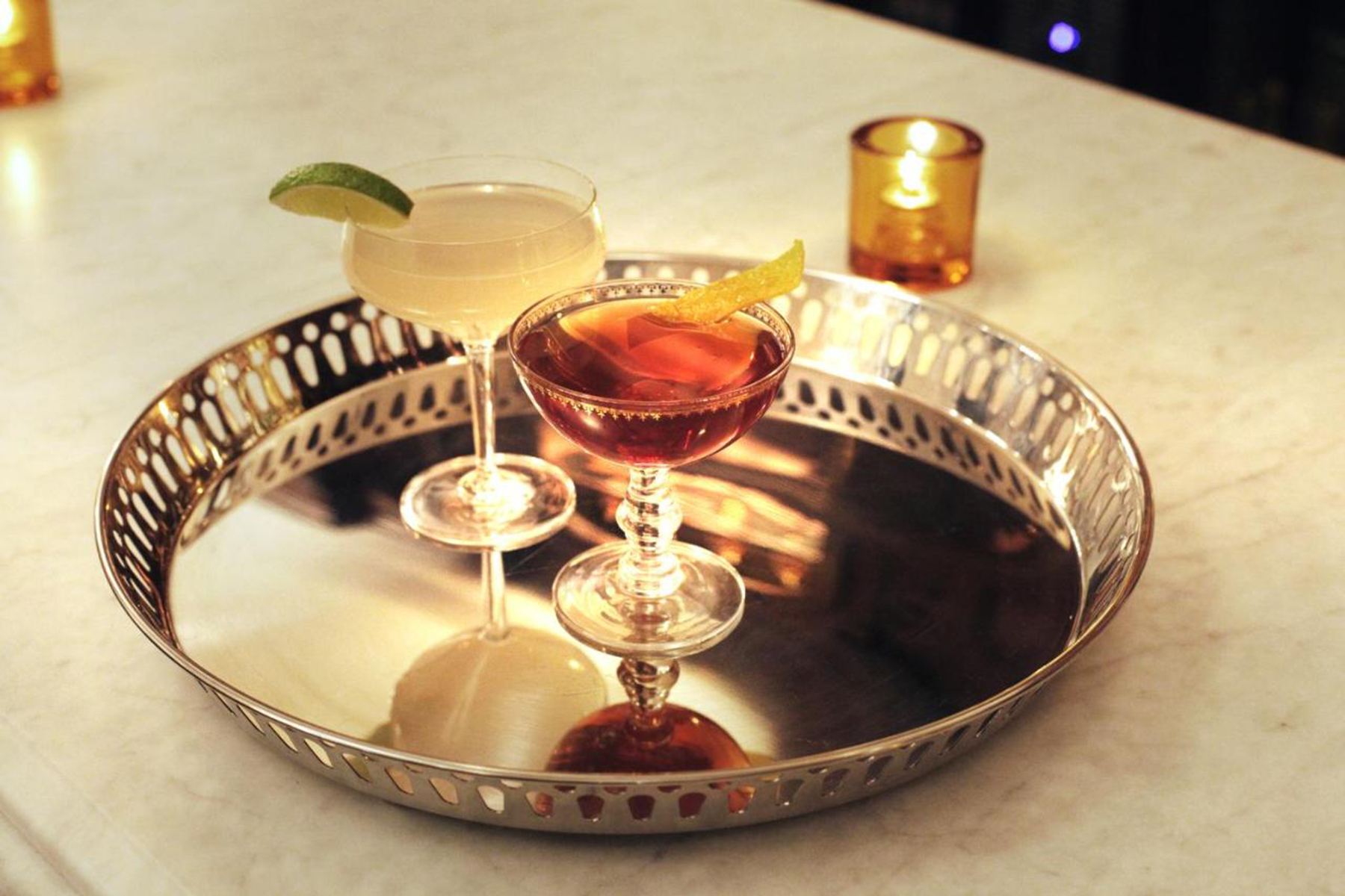 Two cocktails on a silver tray with a lit candle