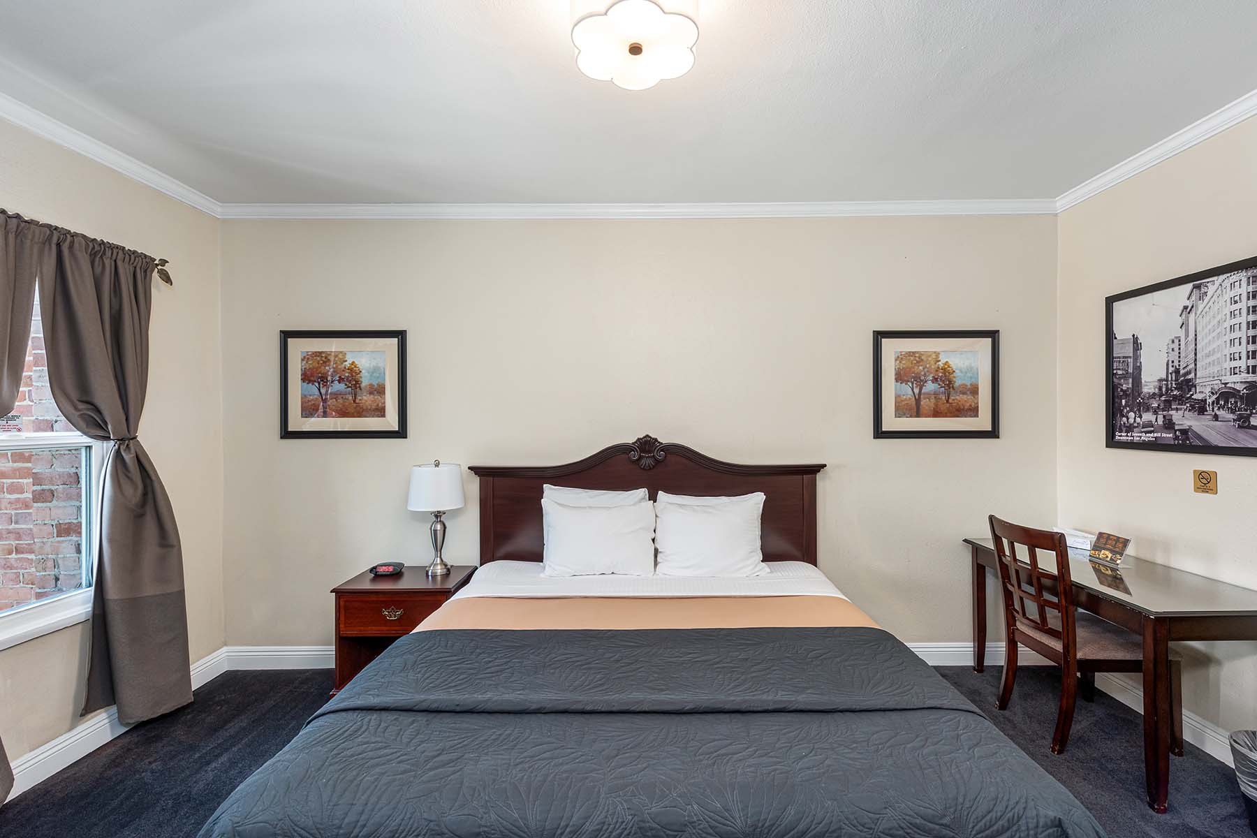 A hotel room with a bed, desk, nightstand, and artwork on the walls.