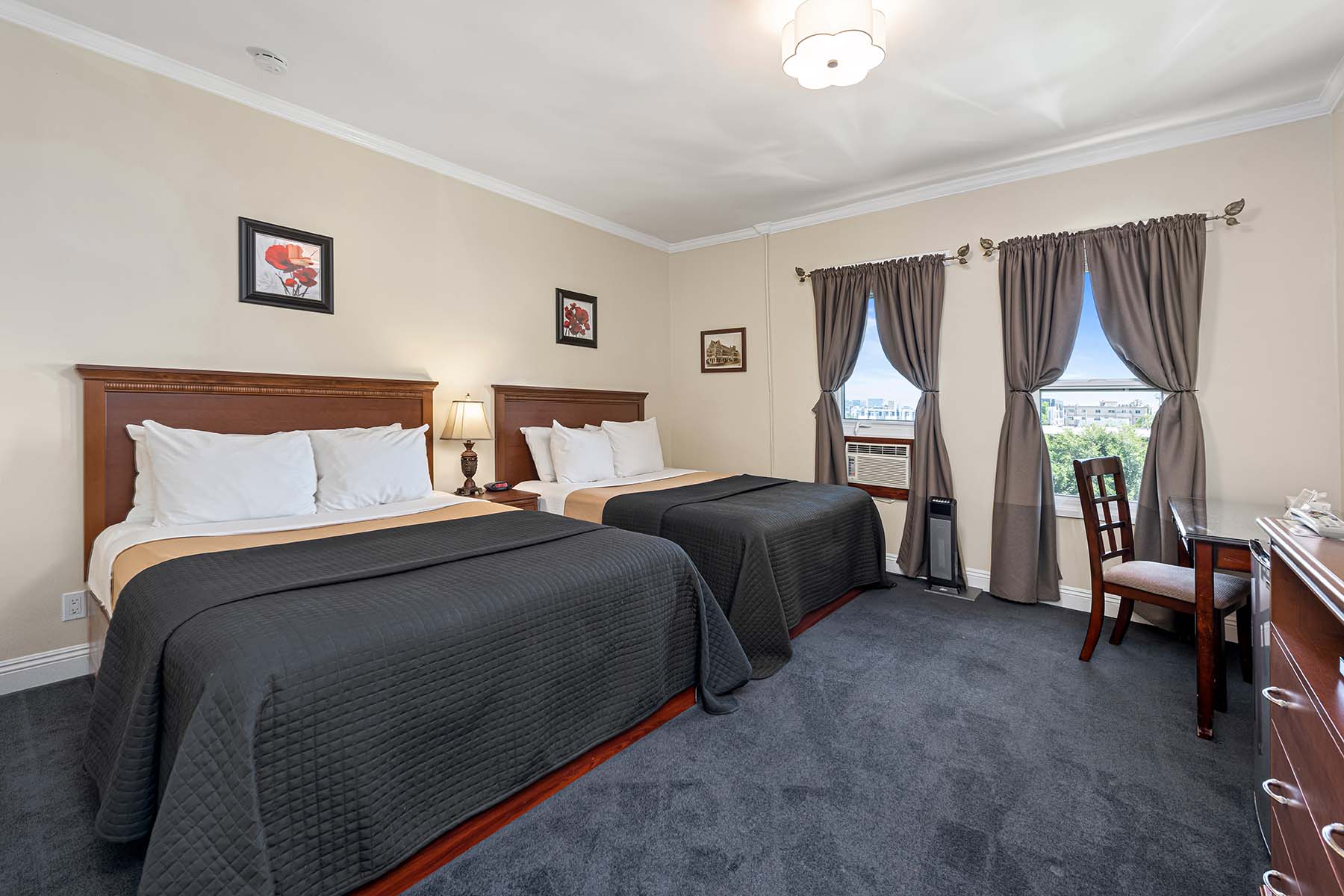 A hotel room with two beds, a desk, and a window.